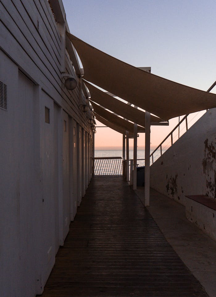 gallery-6 A serene coastal walkway leading to the ocean with a beautiful sunset on the horizon.