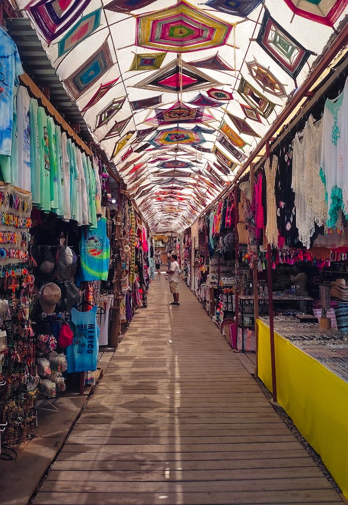contact-img Explore a traditional Mexican market alley filled with colorful textiles, crafts, and a vibrant canopy overhead.
