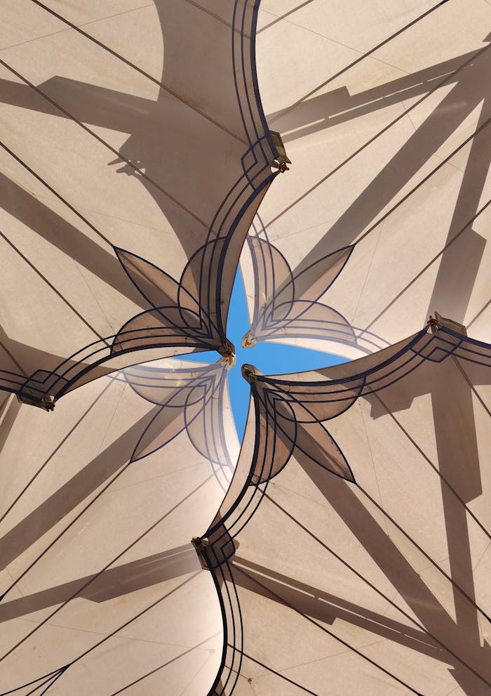 about-01 Intricate ceiling design with geometric patterns and a glimpse of blue sky.