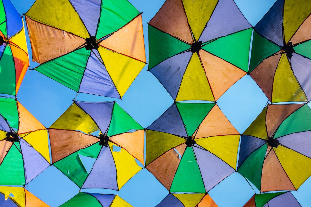 why-choose-us A vibrant array of worn, colorful umbrellas creates a patchwork canopy against a bright blue sky.