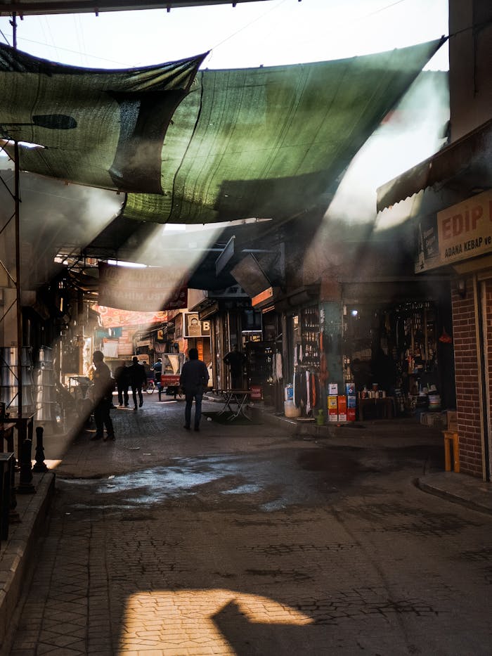 gallery-1 A vibrant marketplace with shops illuminated by dramatic sunlight beams through fabric canopies.